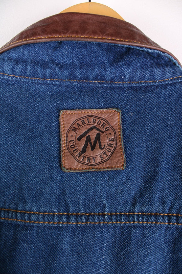 Vintage Marlboro Classics Country Store denim jacket in a indigo blue colourway,The jacket has a leather collar, has a checked cotton flannel yoke on the interior and multiple pockets. There is also a small leather patch sewn onto the back yoke. 