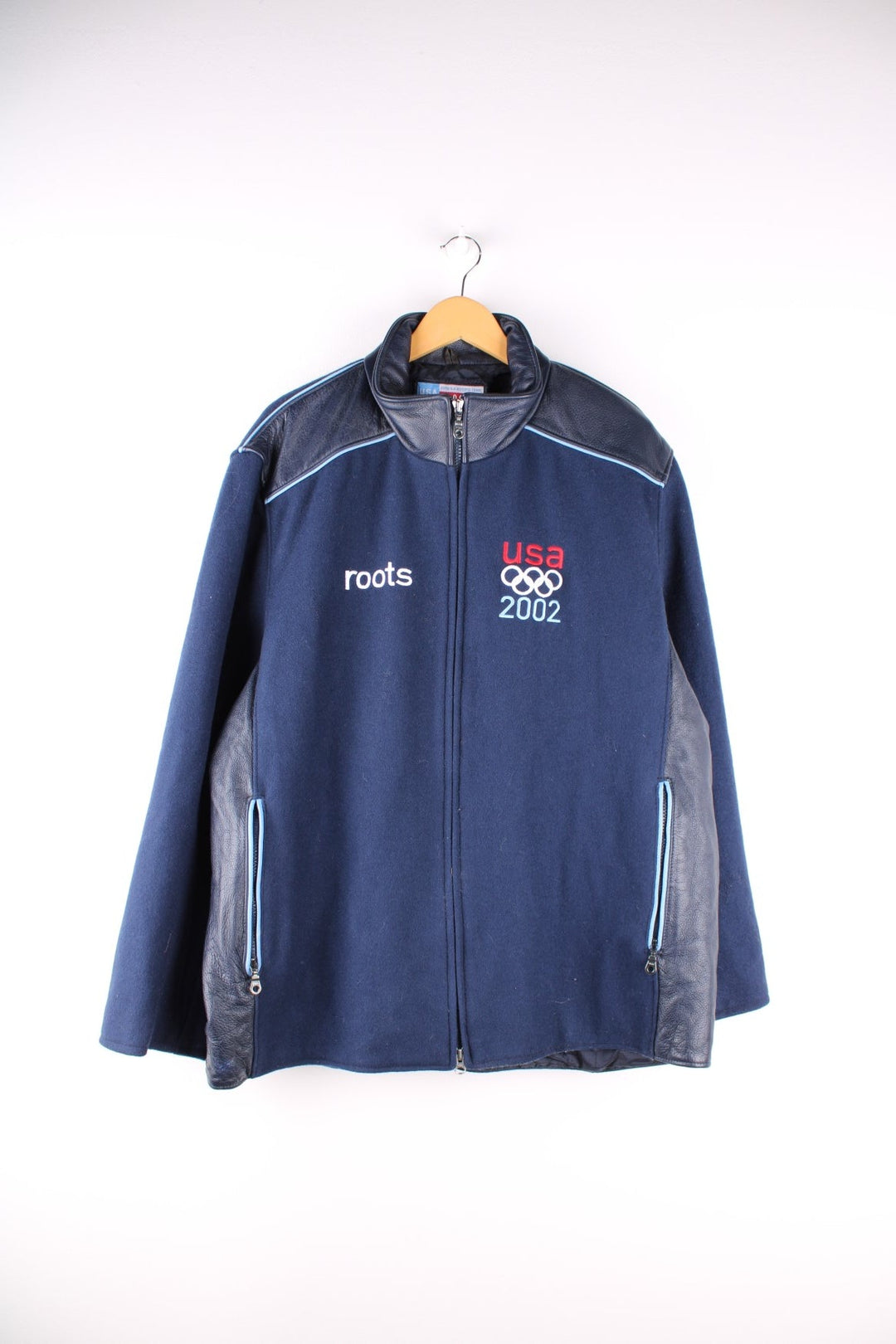 Vintage 2002 USA Winter Olympic Team Coat in a navy blue colourway. The jacket is wool, and has leather patches on the shoulders and side panels. There is a light blue piping on the shoulders too. There are multiple zip pockets on the front and sleeves, embroidered logo on the front, and a large USA flag embroidered on the back. The games took place in Salt Lake City Utah, and was the US's most successful winter games on record, winning 34 medals in total. 