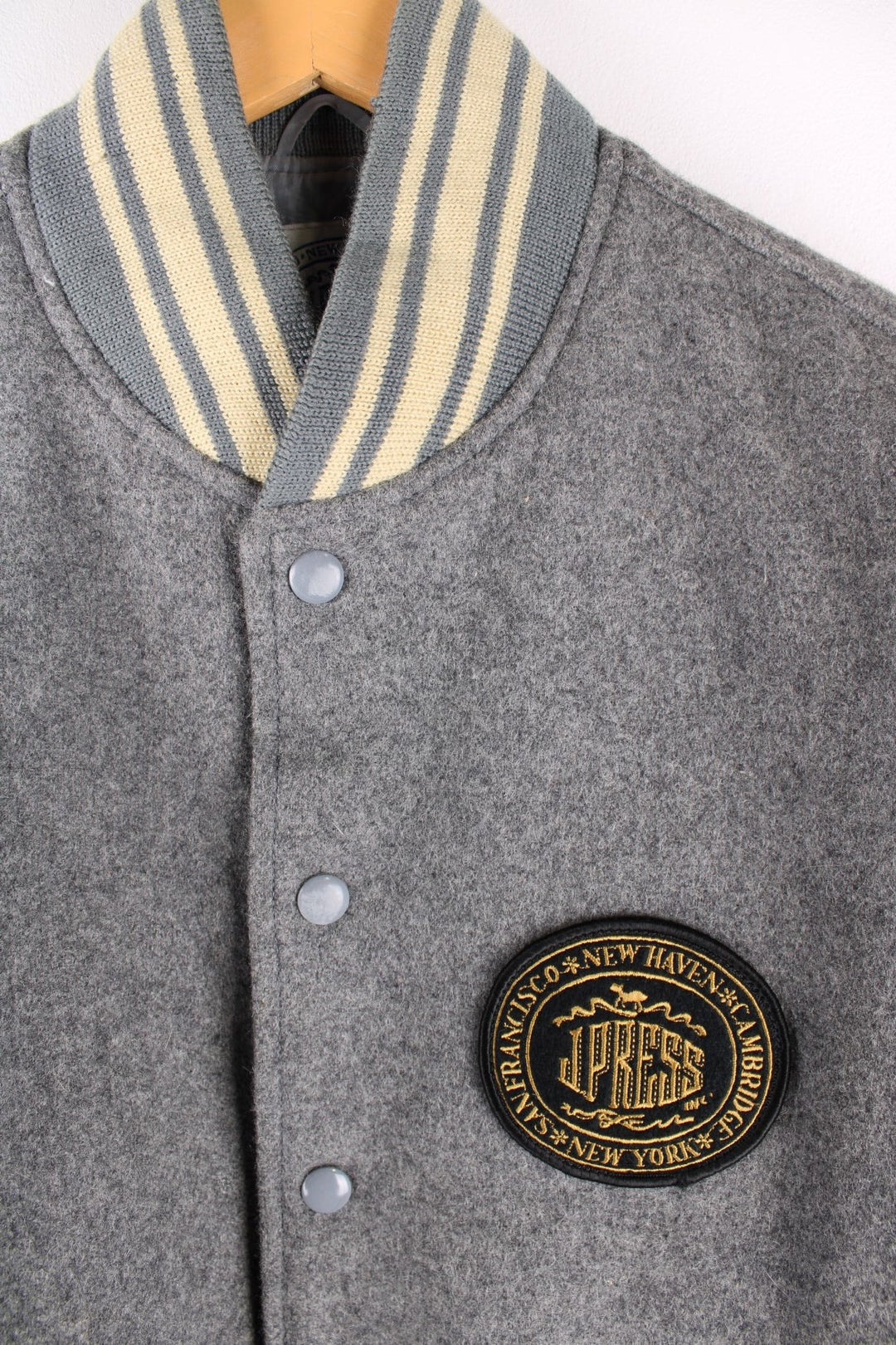 Vintage J Press wool varsity jacket in grey with cream leather sleeves and detailing. The jacket has an elasticated collar and cuffs, jetted pockets and press studs to close. There is a small embroidered patch on the front with a J. Press logo. 