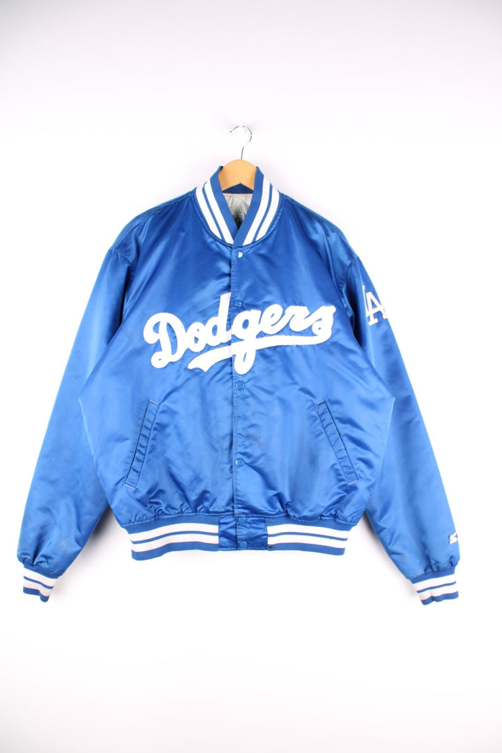 Vintage LA Dodgers baseball jacket in a blue satin colourway. The jacket has the classic elasticated cuffs and collar, press studs to close and was made by Starter, as a part of their Diamond collection and is dated to the 1990S. 