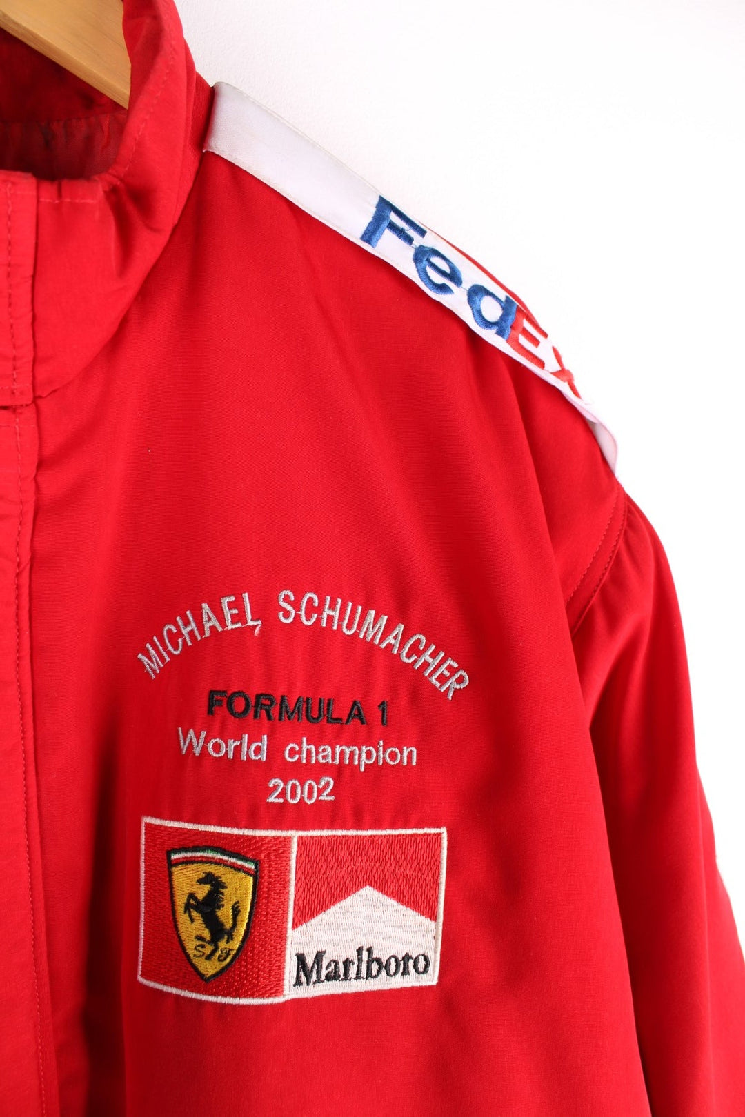 Vintage 2002 Michael Schumacher F1 souvenir jacket in a Ferrari red colourway. The jacket has multiple brand patches down the sleeves, Fed Ex shoulder lapels and a zip/velcro fastening to close. It has a large Marlboro/ Ferrari patch on the back which has to be the most iconic brand collaboration in F1 history. The jacket is dated to 2002, when Schumacher won 11 out of 17 races during the racing season and finished on the podium for all 17. 