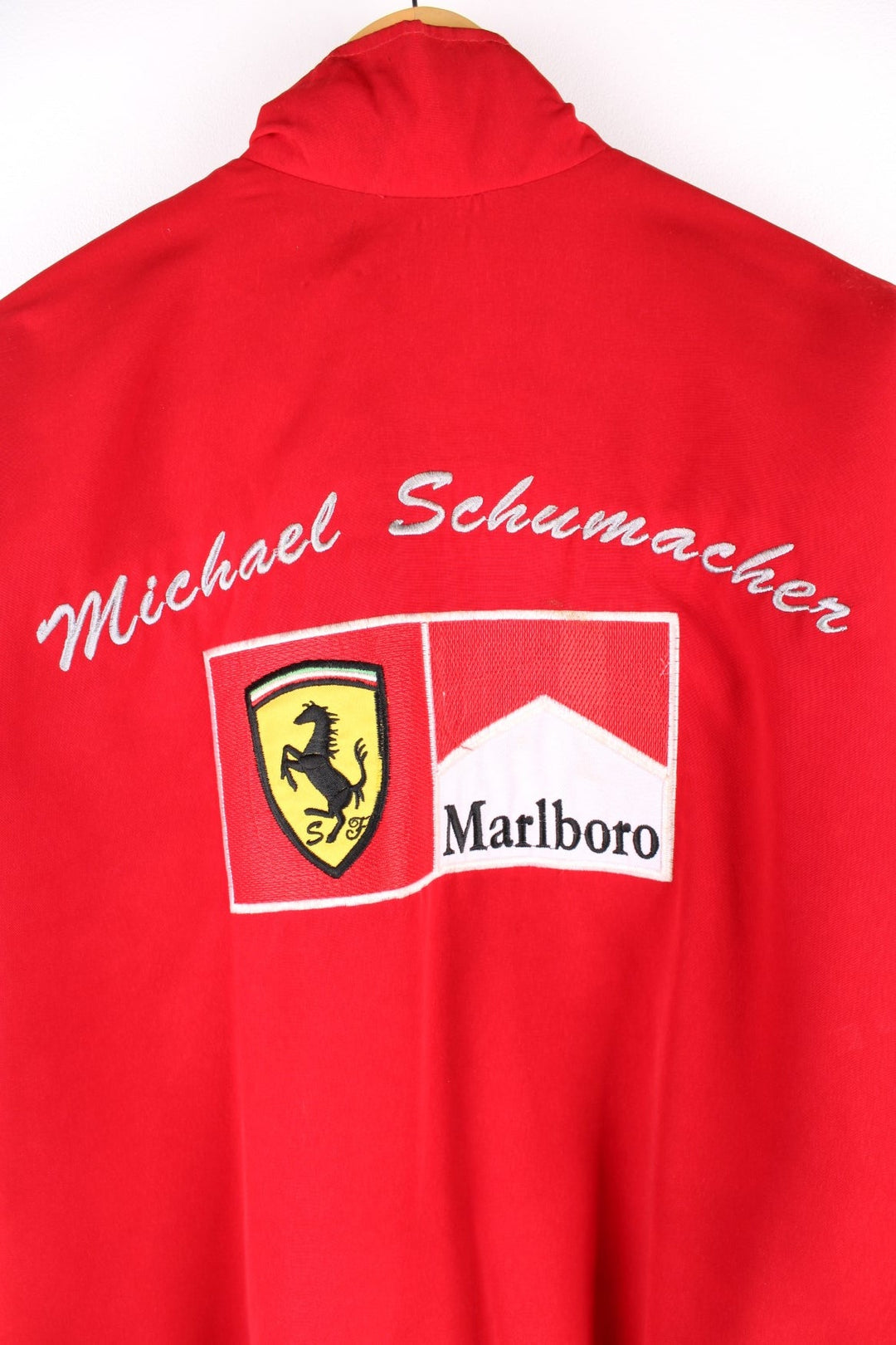 Vintage 2002 Michael Schumacher F1 souvenir jacket in a Ferrari red colourway. The jacket has multiple brand patches down the sleeves, Fed Ex shoulder lapels and a zip/velcro fastening to close. It has a large Marlboro/ Ferrari patch on the back which has to be the most iconic brand collaboration in F1 history. The jacket is dated to 2002, when Schumacher won 11 out of 17 races during the racing season and finished on the podium for all 17. 