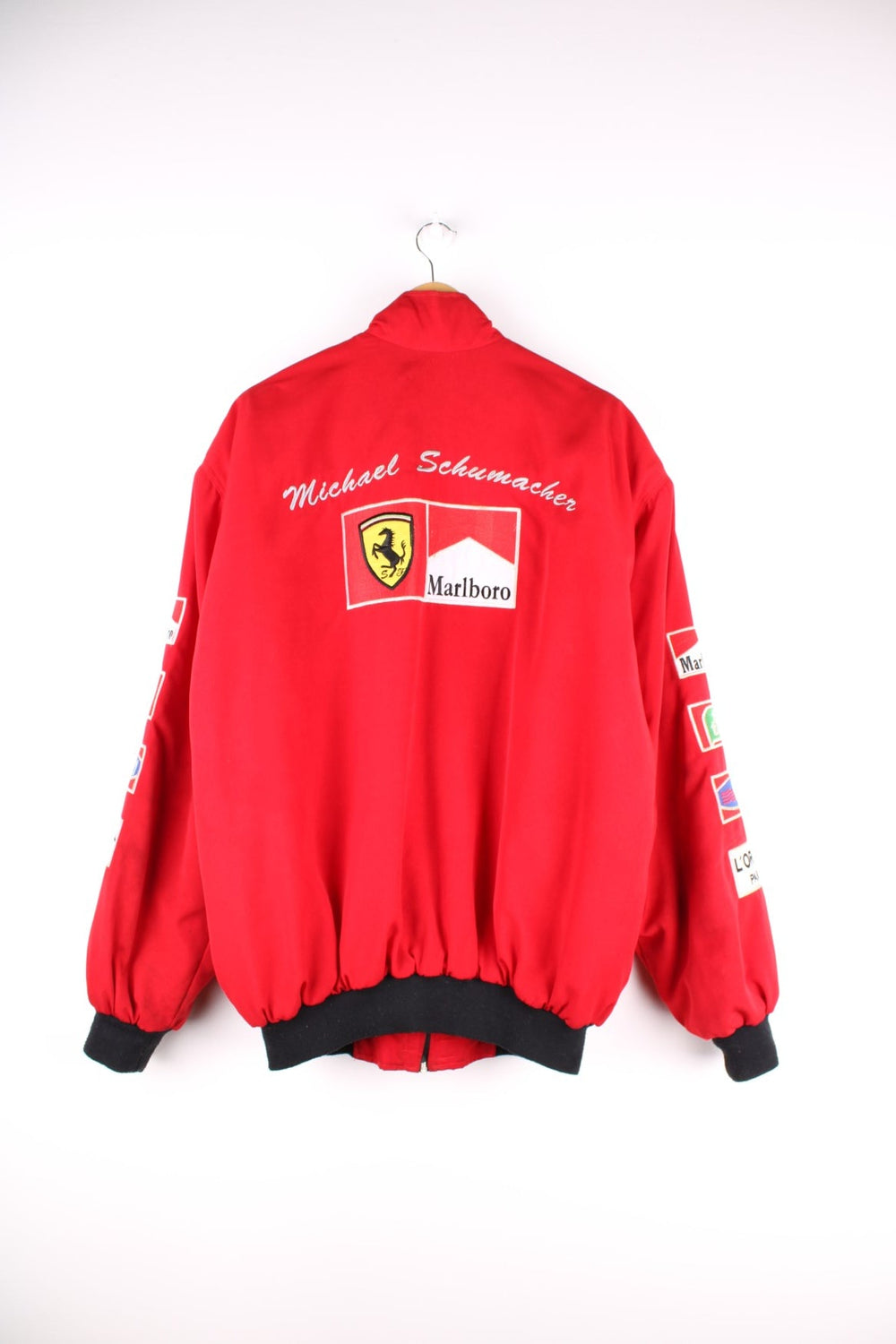 Vintage 2002 Michael Schumacher F1 souvenir jacket in a Ferrari red colourway. The jacket has multiple brand patches down the sleeves, Fed Ex shoulder lapels and a zip/velcro fastening to close. It has a large Marlboro/ Ferrari patch on the back which has to be the most iconic brand collaboration in F1 history. The jacket is dated to 2002, when Schumacher won 11 out of 17 races during the racing season and finished on the podium for all 17. 