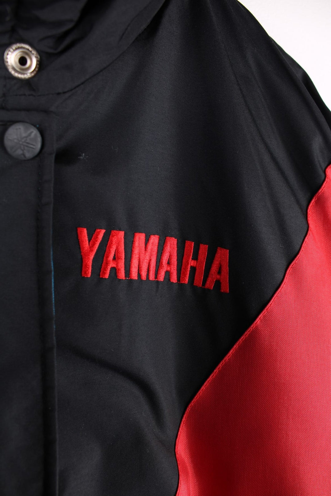 Vintage Yamaha motorcycle jacket in a black, blue and red colourway, the jacket is quilted, has an elasticated hem and interior pocket. It has flashes of red and blue and a large YAMAHA logo embroidered on the back. There is also a small metal Yamaha lgo pinned to the front. Dates to the 1990s. 