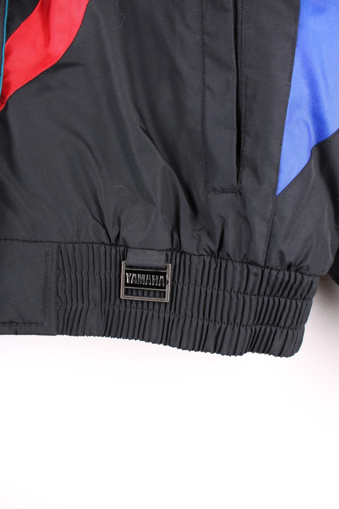 Vintage Yamaha motorcycle jacket in a black, blue and red colourway, the jacket is quilted, has an elasticated hem and interior pocket. It has flashes of red and blue and a large YAMAHA logo embroidered on the back. There is also a small metal Yamaha lgo pinned to the front. Dates to the 1990s. 