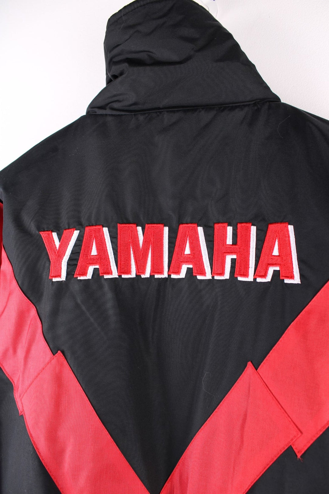 Vintage Yamaha motorcycle jacket in a black, blue and red colourway, the jacket is quilted, has an elasticated hem and interior pocket. It has flashes of red and blue and a large YAMAHA logo embroidered on the back. There is also a small metal Yamaha lgo pinned to the front. Dates to the 1990s. 