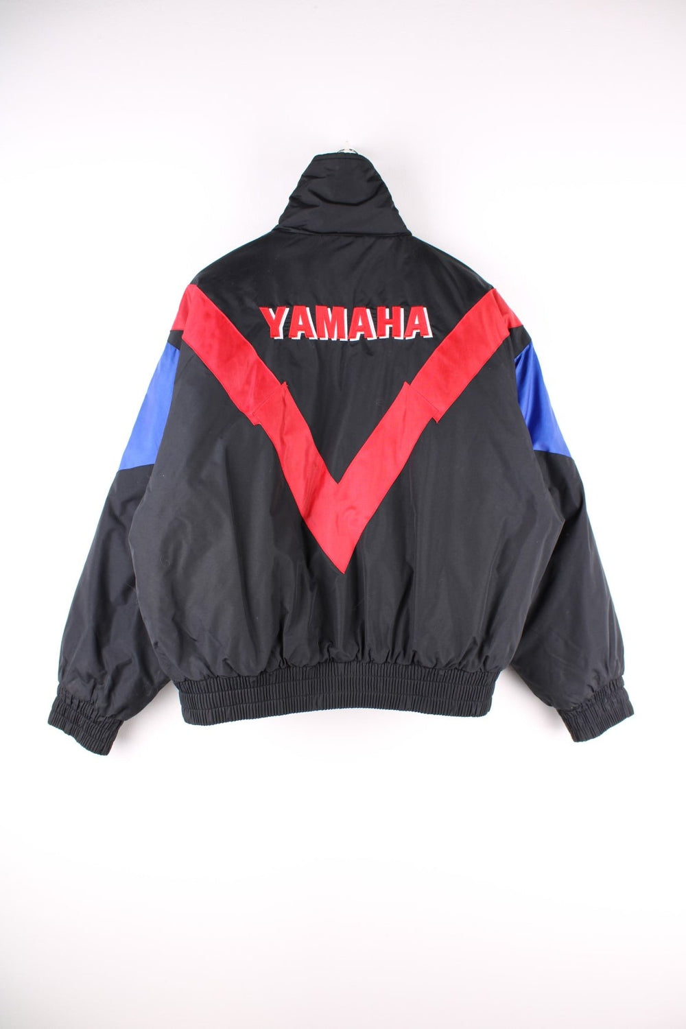 Vintage Yamaha motorcycle jacket in a black, blue and red colourway, the jacket is quilted, has an elasticated hem and interior pocket. It has flashes of red and blue and a large YAMAHA logo embroidered on the back. There is also a small metal Yamaha lgo pinned to the front. Dates to the 1990s. 