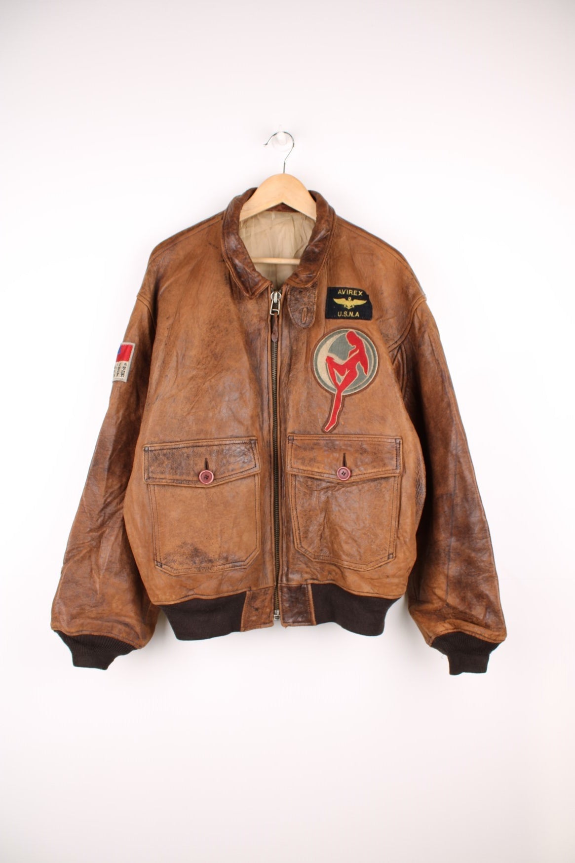 Vintage Avirex Flight Aviator Bomber Jacket in a brown colourway, zip up with side pockets and has badges embroidered on the front alongside the Avirex logo. 