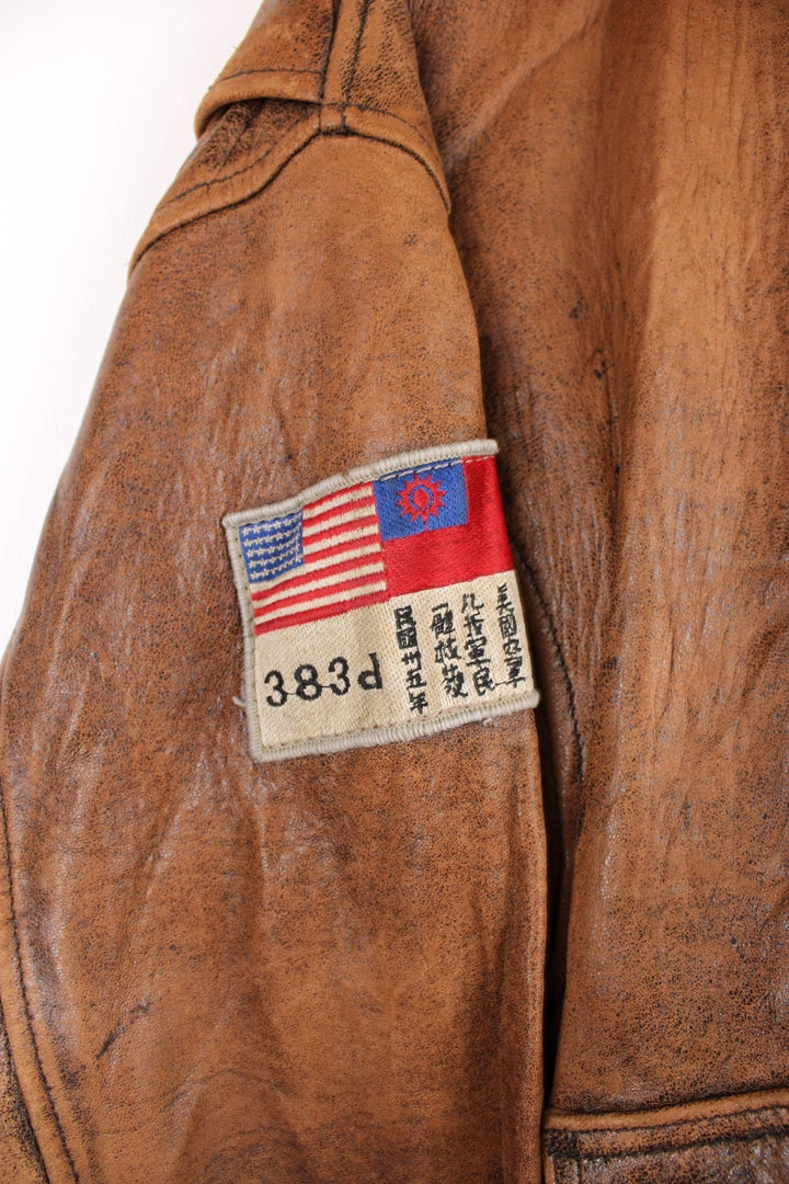 Vintage Avirex Flight Aviator Bomber Jacket in a brown colourway, zip up with side pockets and has badges embroidered on the front alongside the Avirex logo. 