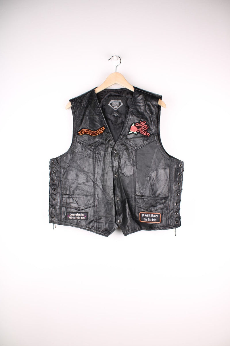 Leather Biker Vest in a black colourway, button up with a v neck collar, and has multiple patches embroidered around the gilet. 