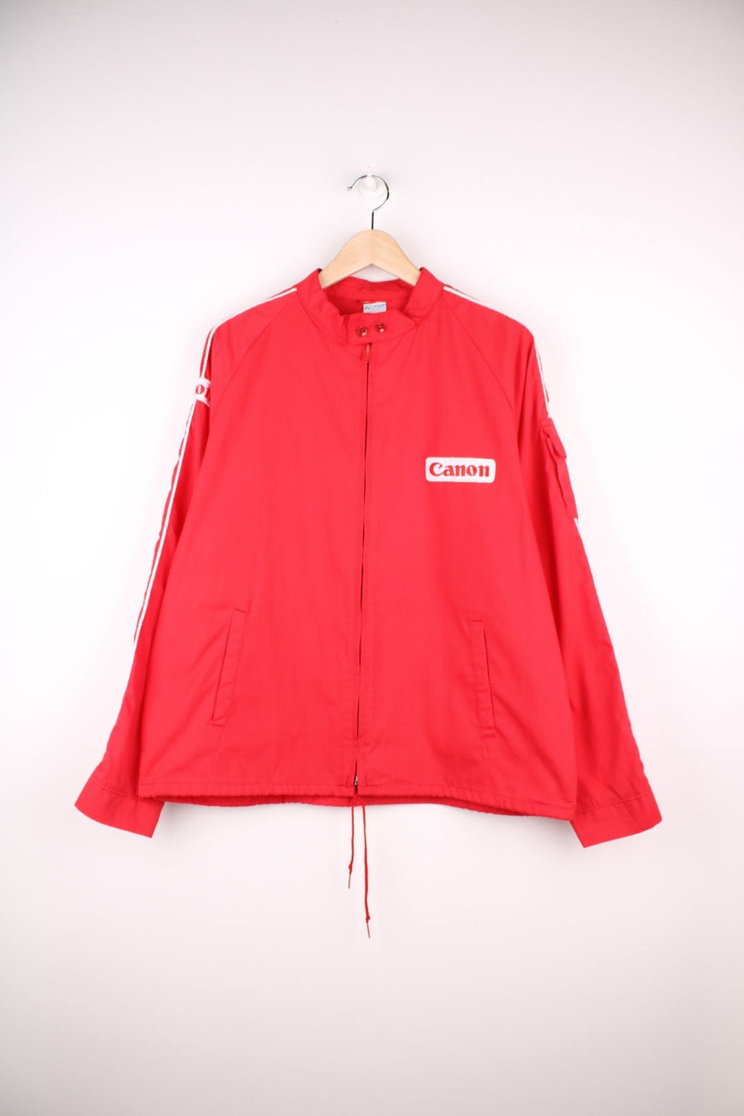 1983 Canon lightweight jacket in red with white piping, embroidered logos, a drawstring at the waist, zip closure and a back graphic of a hot air balloon and text reading 'Albuquerque International Balloon Fiesta - 200 Years of Flight'. 