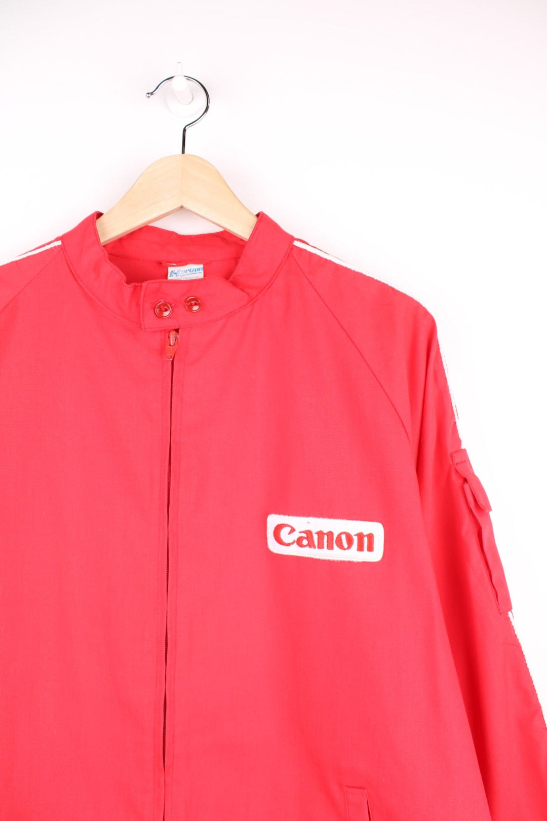 1983 Canon lightweight jacket in red with white piping, embroidered logos, a drawstring at the waist, zip closure and a back graphic of a hot air balloon and text reading 'Albuquerque International Balloon Fiesta - 200 Years of Flight'. 