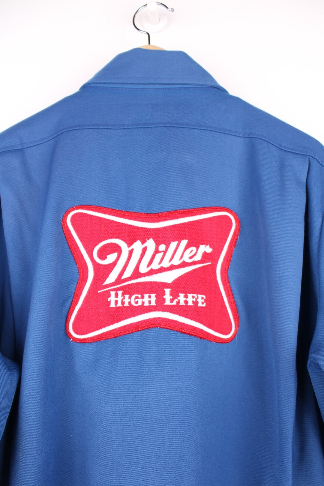 60s Miller beer lightweight delivery jacket in blue with assorted Miller beer patches on the back, ches, and sleeves, zip closure, two pockets, and the name Ralph embroidered in red on the front. 