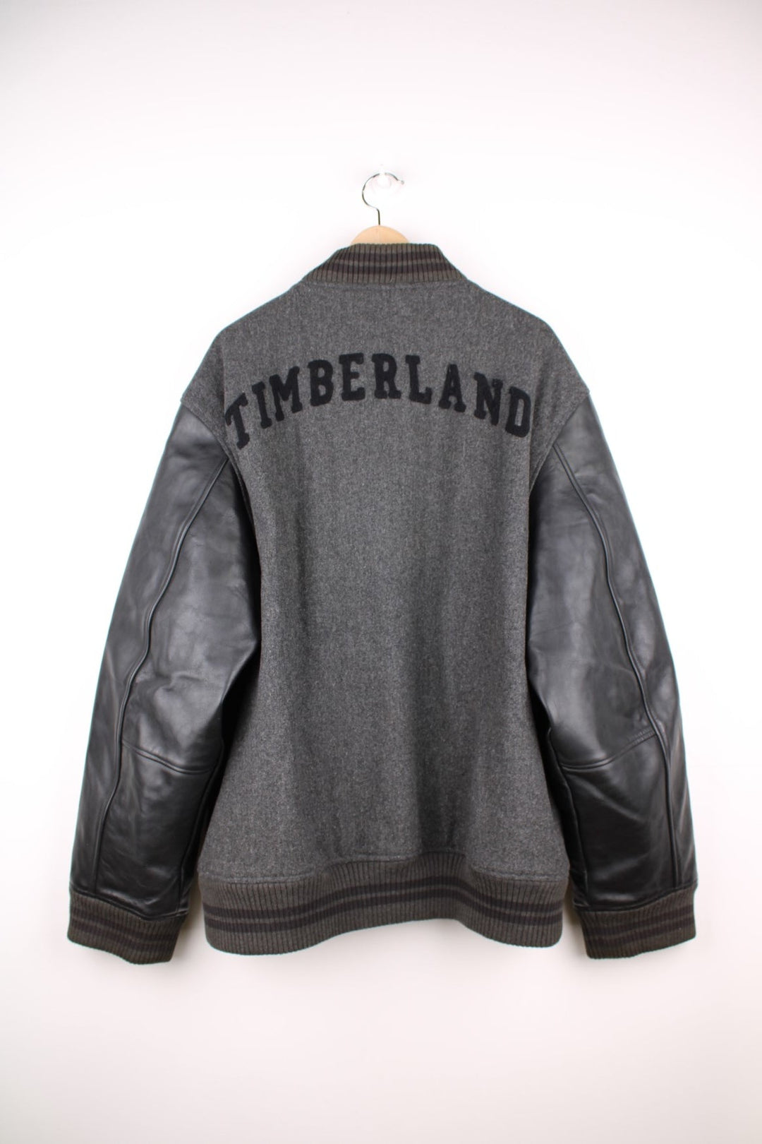 Timberland varsity jacket in a grey wool blend with 100% leather sleeves, two pockets, an embroidered tree logo on the front and spellout on the book. 