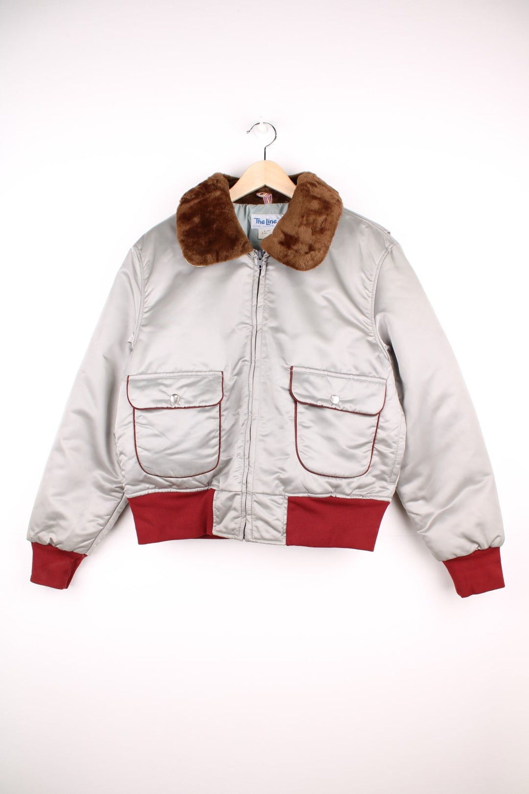 The Line' Denver, Colorado bomber-style goose down ski jacket in silvery grey with red piping, hem and cuffs, a faux fur collar, zip closure and two pockets.