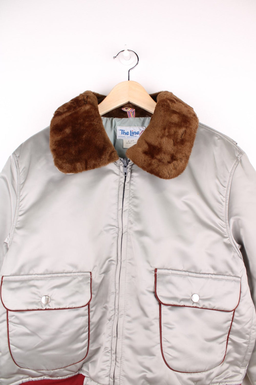 The Line' Denver, Colorado bomber-style goose down ski jacket in silvery grey with red piping, hem and cuffs, a faux fur collar, zip closure and two pockets.