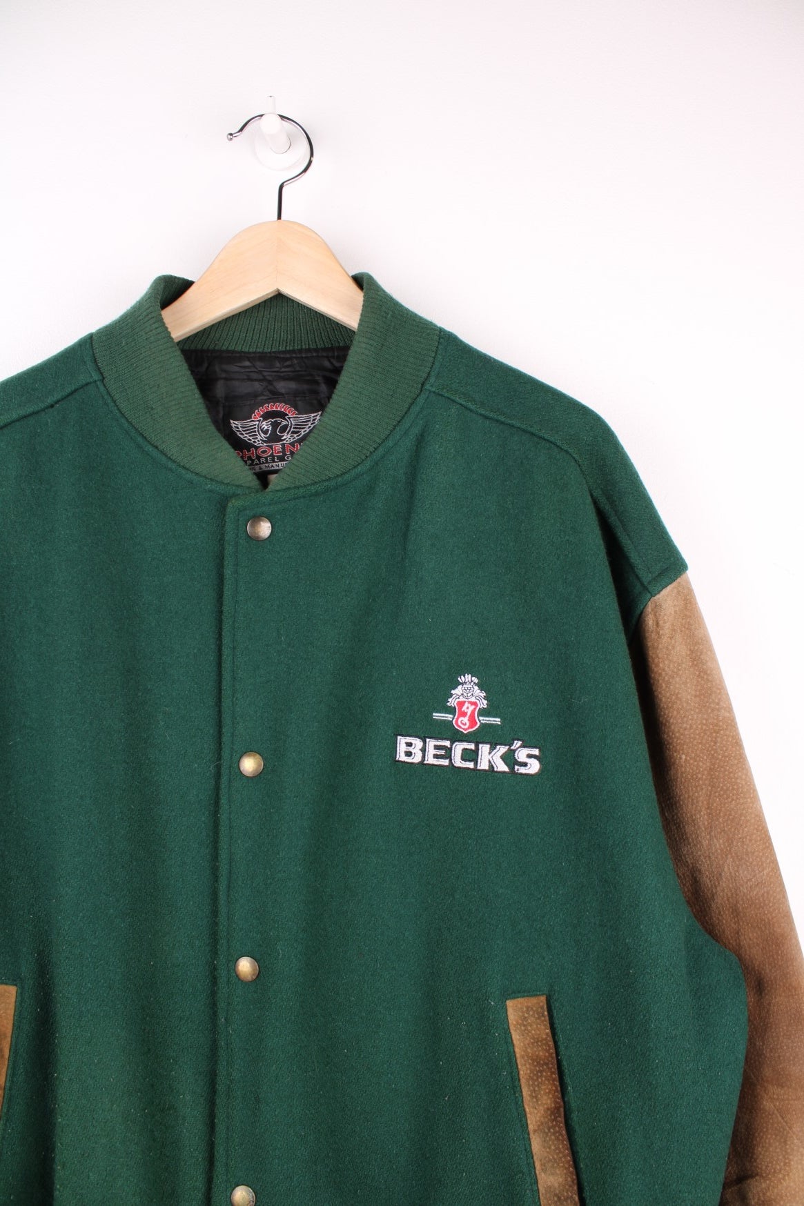 Becks Beer Varsity Jacket in a green and brown colourway, button up and has side pockets, insulated with a quilted lining, and has the logo embroidered on the front.