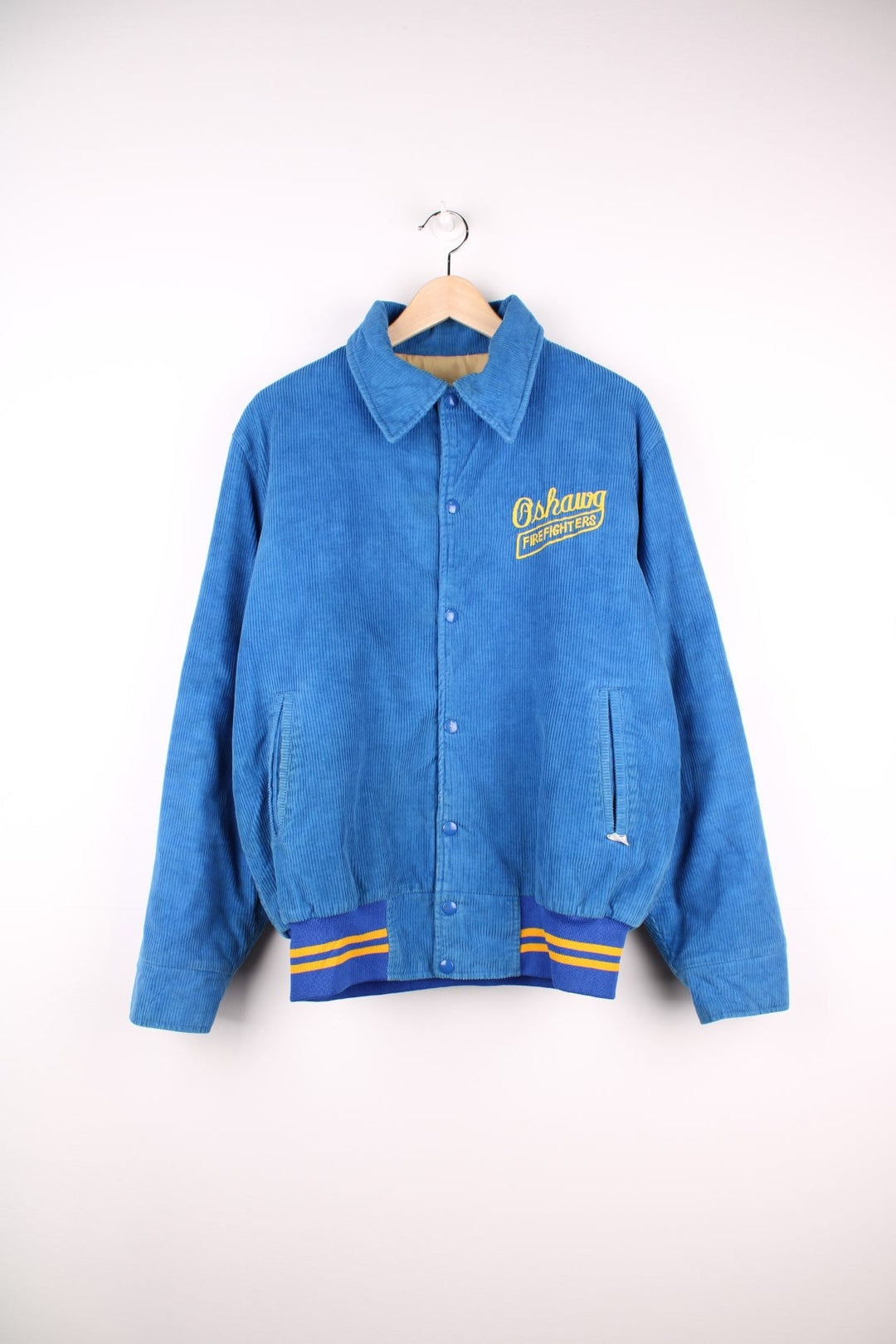 Vintage 80's Oshawa Firefighters Corduroy Varsity Jacket in a blue and yellow colourway, buttons up and has side pockets, insulated with a quilted lining, and has the logos embroidered on the front and right sleeve.