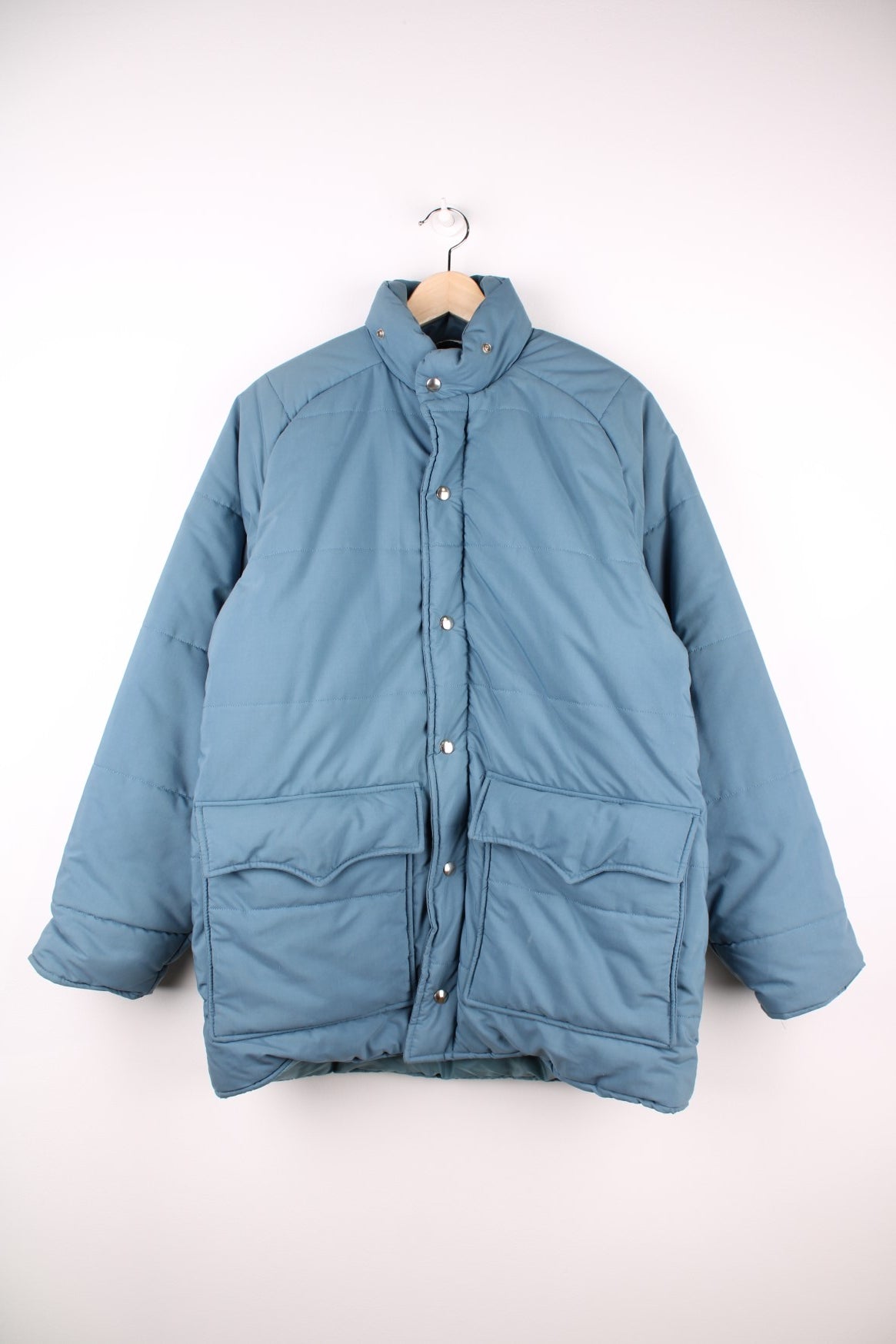 Woolrich Down Puffer Coat in a blue colourway, zips and buttons up, has double pockets on the front and insulated with a quilted lining. 