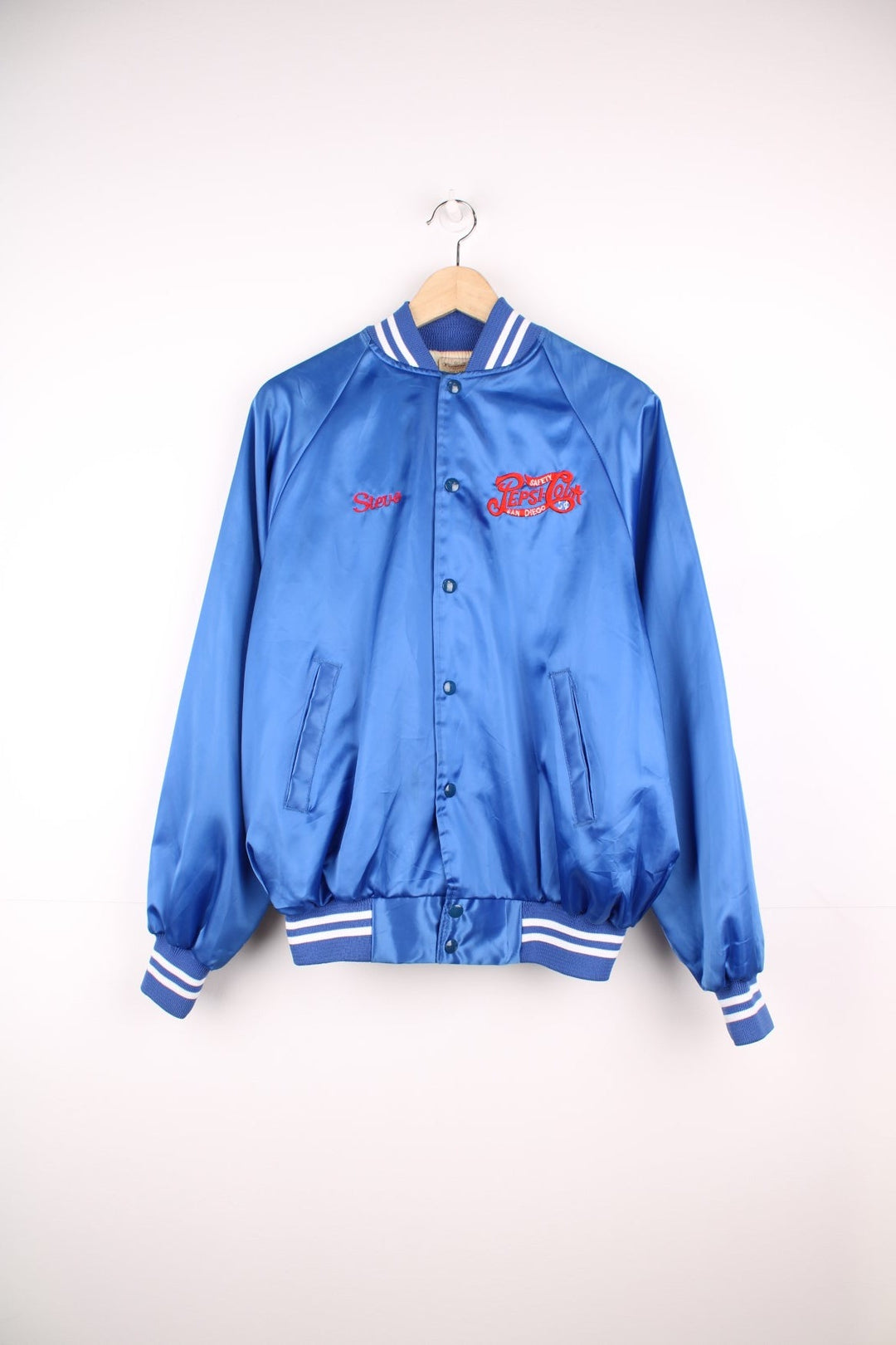 Blue 'Pepsi-Cola' personalised bomber jacket with white striped accents around the collar and cuffs. Snap closure, with the Pepsi-Cola logo embroidered on the chest and back. 