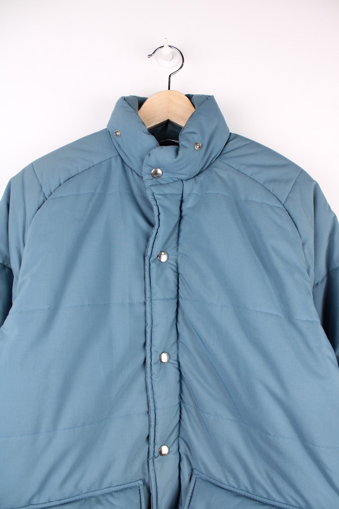 Woolrich Down Puffer Coat in a blue colourway, zips and buttons up, has double pockets on the front and insulated with a quilted lining. 