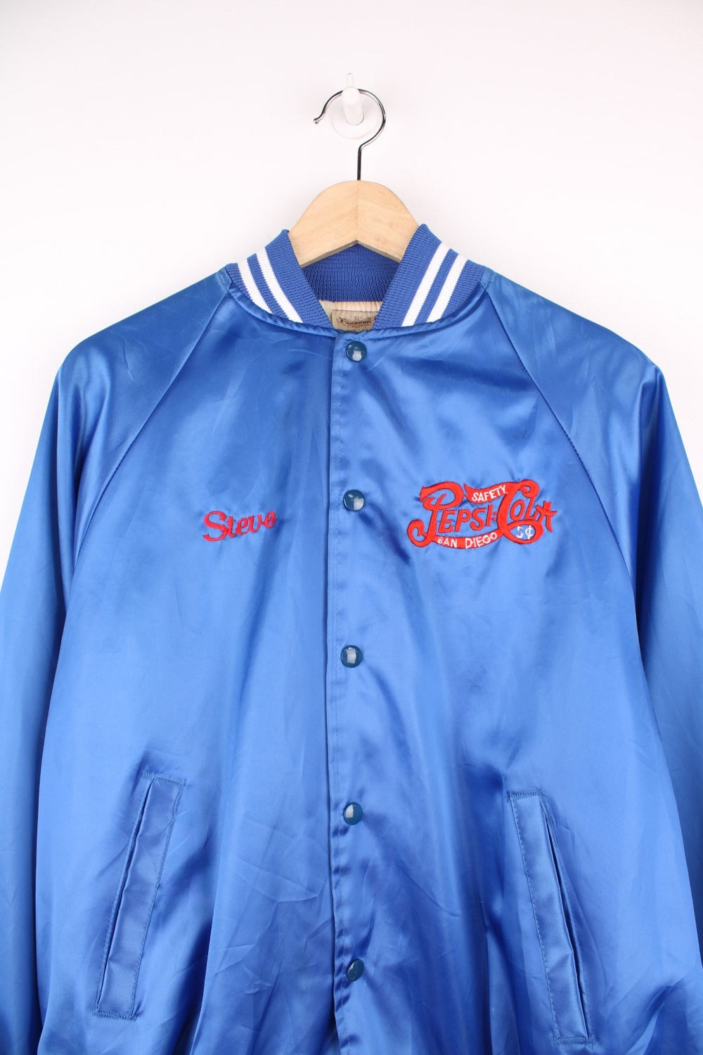 Blue 'Pepsi-Cola' personalised bomber jacket with white striped accents around the collar and cuffs. Snap closure, with the Pepsi-Cola logo embroidered on the chest and back. 