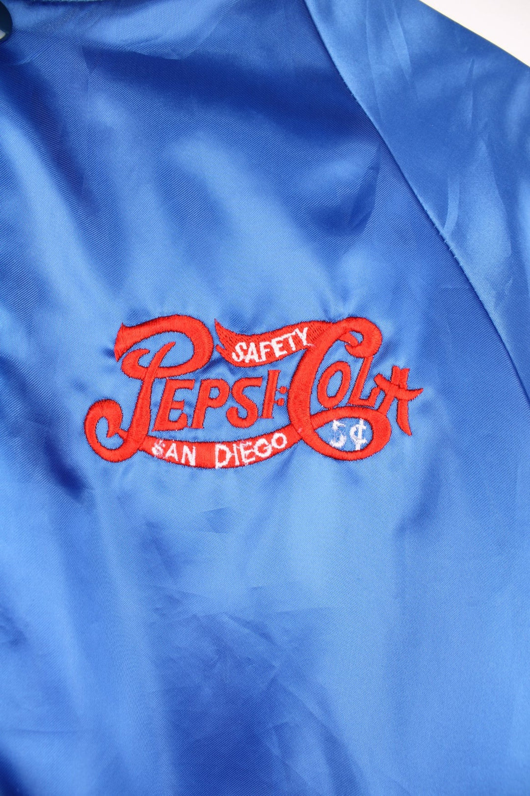 Blue 'Pepsi-Cola' personalised bomber jacket with white striped accents around the collar and cuffs. Snap closure, with the Pepsi-Cola logo embroidered on the chest and back. 