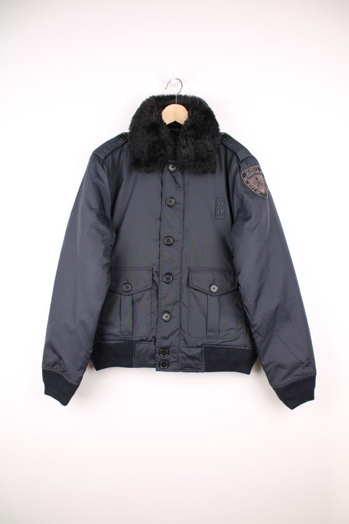 Schott NYC black pilot jacket with a removable faux fur collar, quilt lining, zip and button closure, two buttoned pockets, and epaulette loops on the shoulders. 