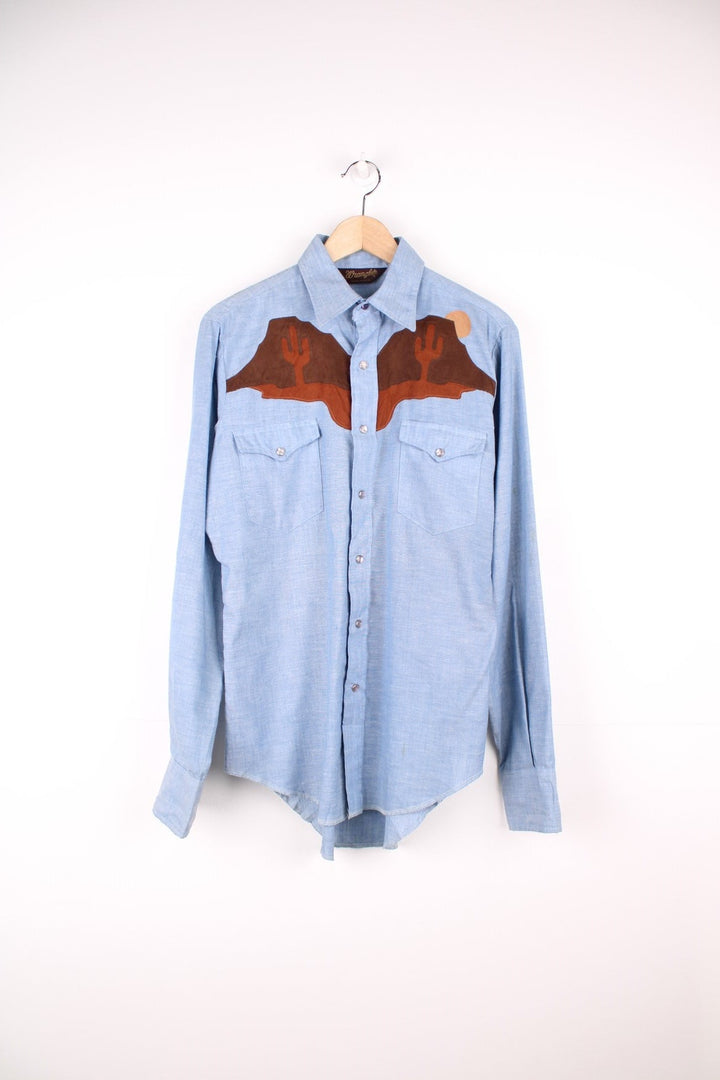 Wrangler Western blue denim shirt with brown suede desert scene yoke on the front and back. Long sleeves, snap closure, and western-style breast pockets. 