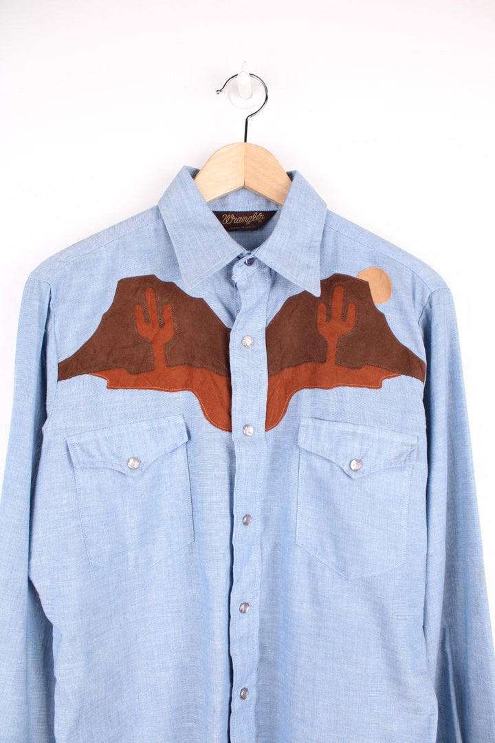 Wrangler Western blue denim shirt with brown suede desert scene yoke on the front and back. Long sleeves, snap closure, and western-style breast pockets. 