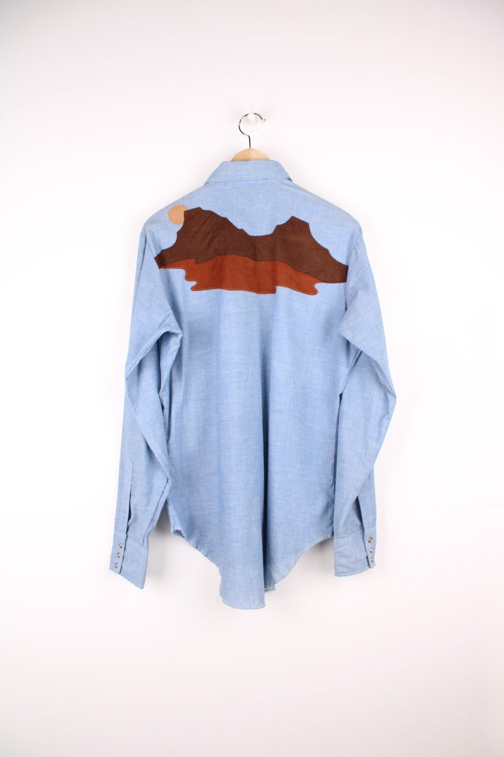 Wrangler Western blue denim shirt with brown suede desert scene yoke on the front and back. Long sleeves, snap closure, and western-style breast pockets. 