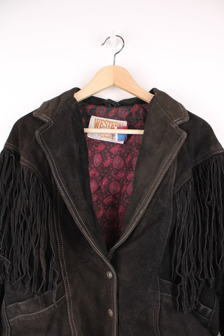 Western by Schott black suede fringe jacket with white contrast stitching, front patch pockets, button closure, a paisley lining, and lace-up detailing on the cuffs and back hem. 