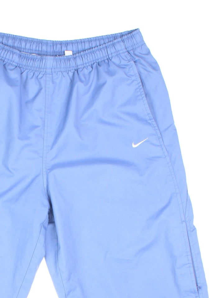 Nike tracksuit bottoms in sky blue with two pockets, an elasticated waistband, and a small embroidered swoosh logo on the front.