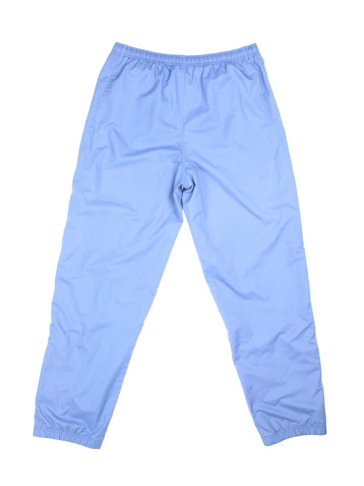 Nike tracksuit bottoms in sky blue with two pockets, an elasticated waistband, and a small embroidered swoosh logo on the front.