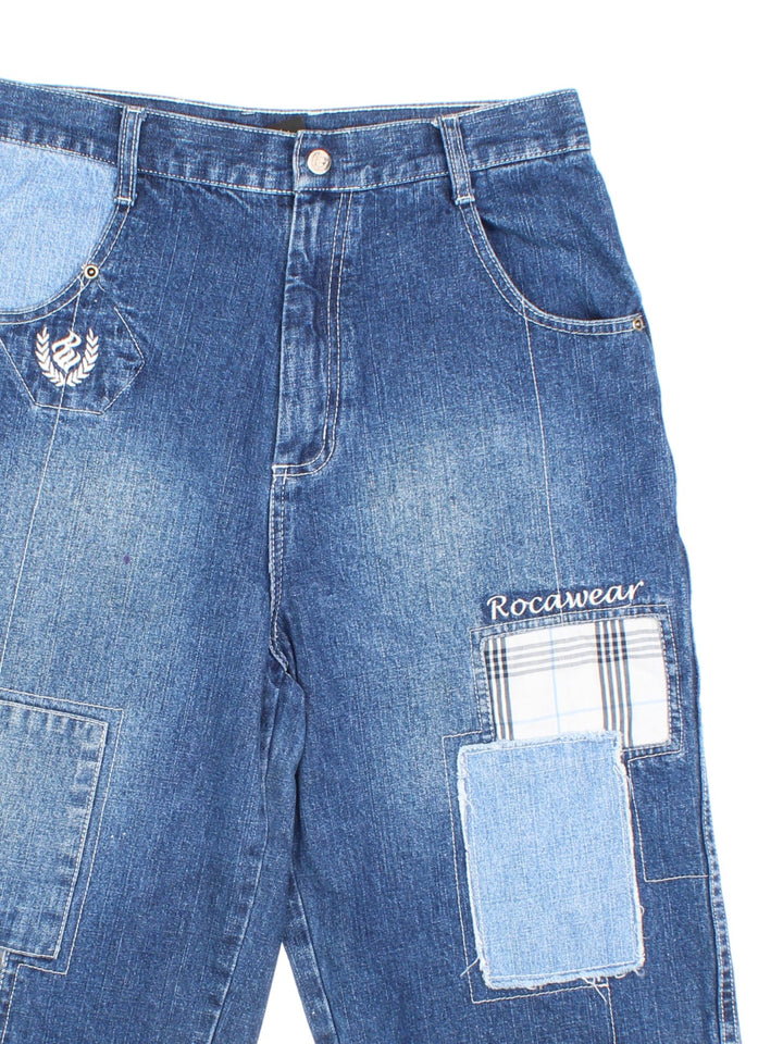 Y2K Rocawear patchwork denim shorts in blue  with four pockets, zip and button closure, several embroidered logos and a logo patch on the back.