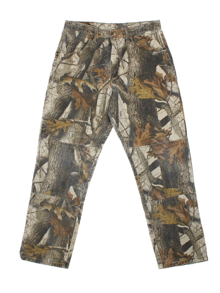 Wrangler Real Tree Camo Jeans in green and brown patterned colourway with multiple pockets, double knee features, and has the logo embroidered on the back.