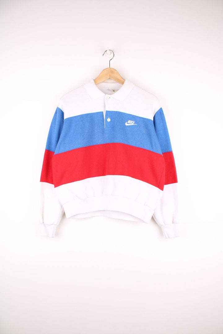 80's Nike Collared Sweatshirt in a white, blue and red block patterned colourway, quarter button up with a collar, and has the logo embroidered on the chest. 