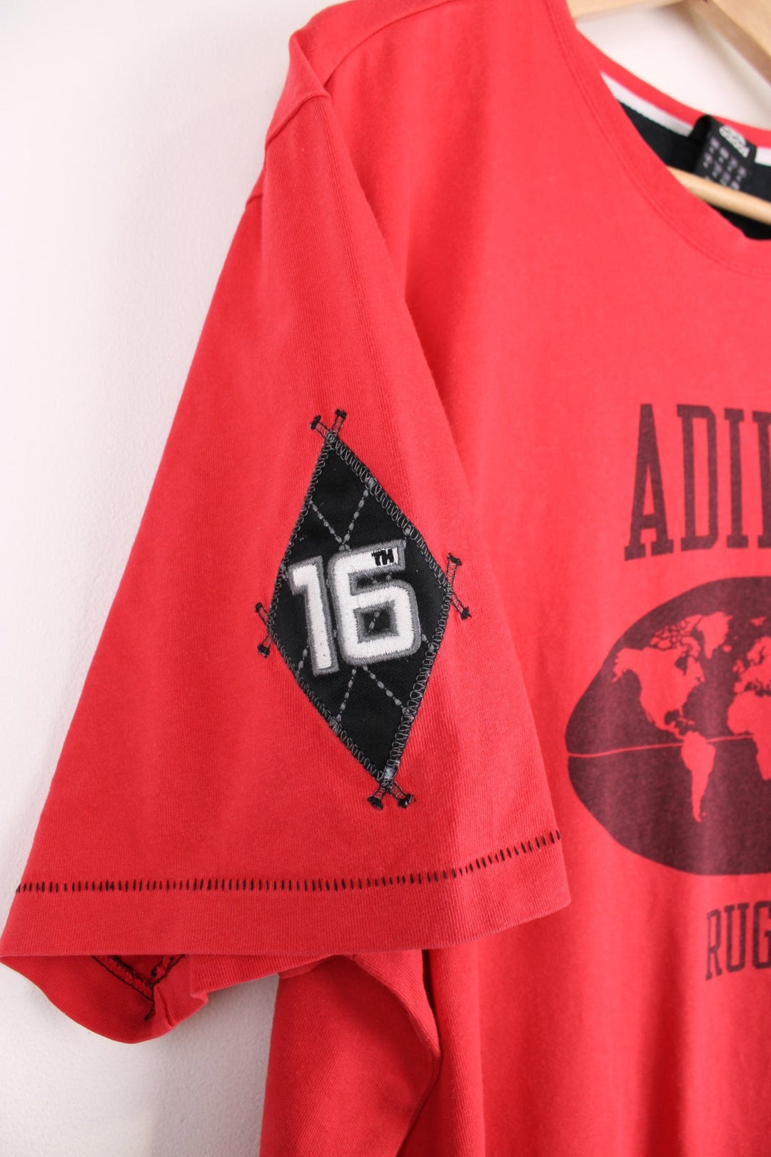 Adidas Rugby T-Shirt in a red and black colourway with the spell out logo and globe graphic printed on the front, and badge logos embroidered on the sleeves. 