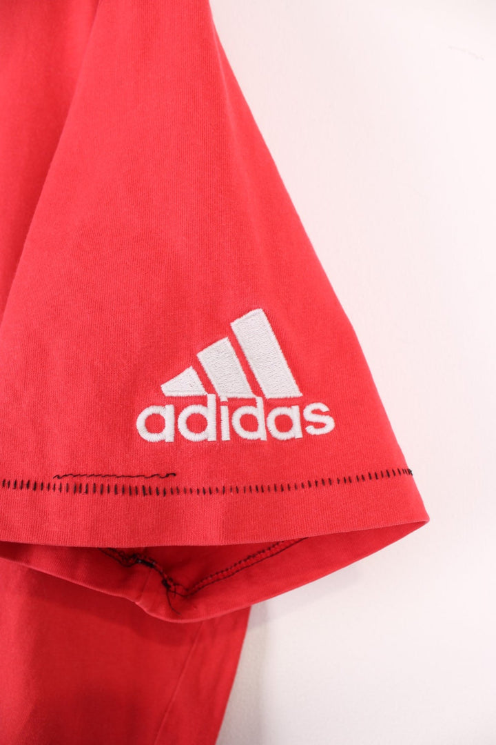 Adidas Rugby T-Shirt in a red and black colourway with the spell out logo and globe graphic printed on the front, and badge logos embroidered on the sleeves. 