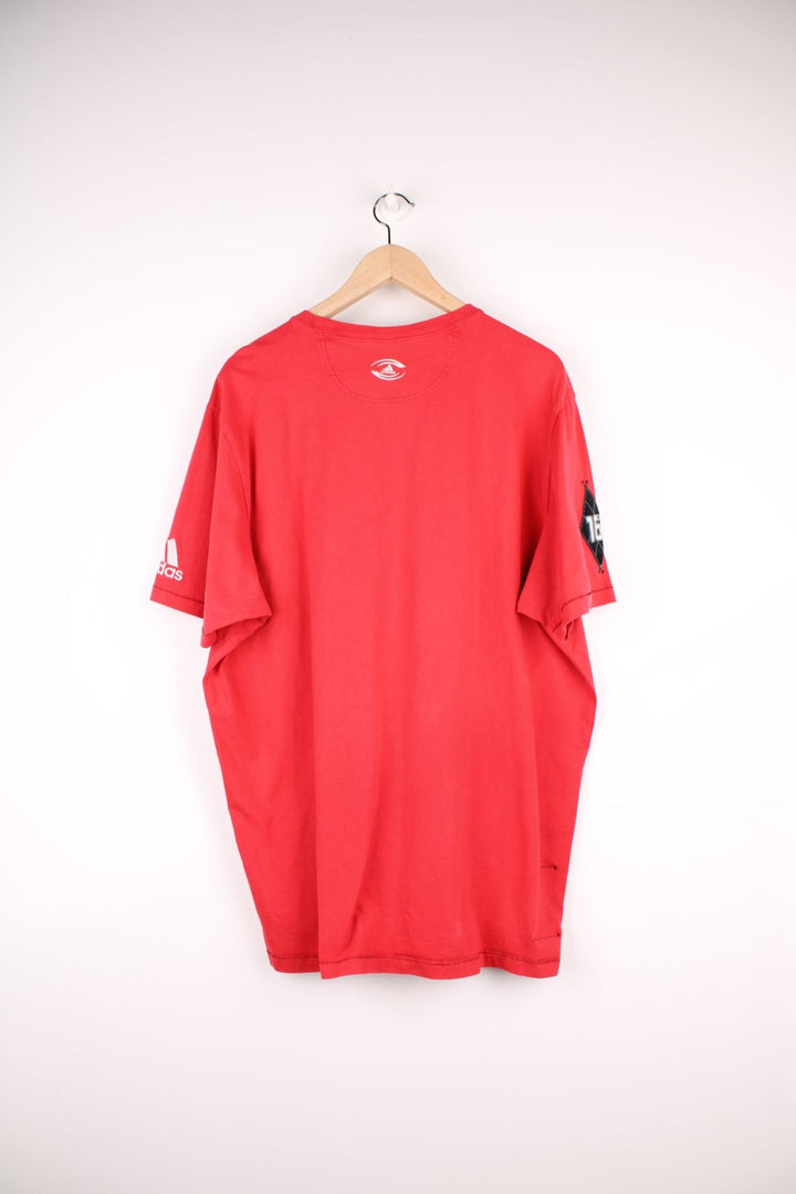 Adidas Rugby T-Shirt in a red and black colourway with the spell out logo and globe graphic printed on the front, and badge logos embroidered on the sleeves. 