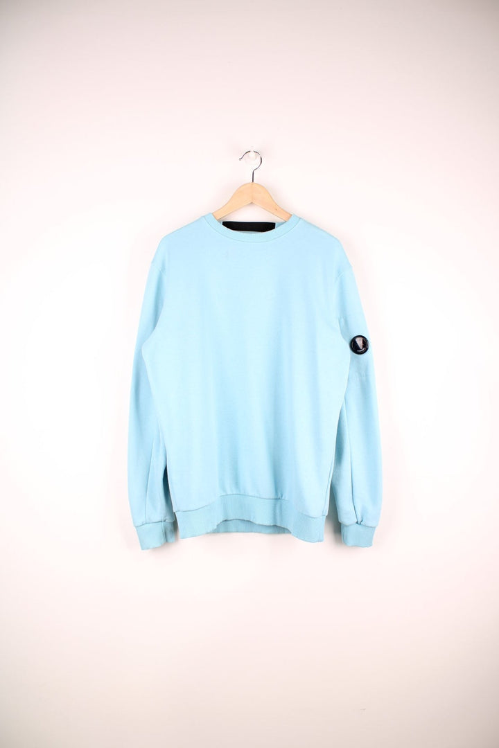 CP Company Sweatshirt in a baby blue colourway, plain crewneck with the google and pocket on the left sleeve.