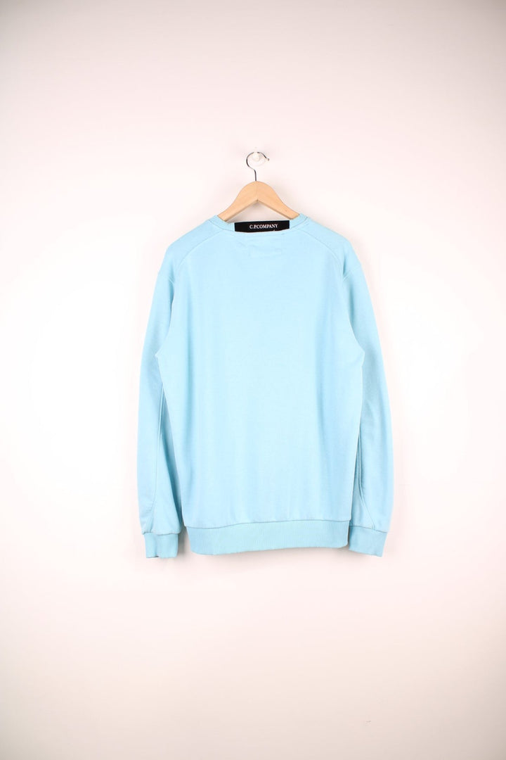 CP Company Sweatshirt in a baby blue colourway, plain crewneck with the google and pocket on the left sleeve.