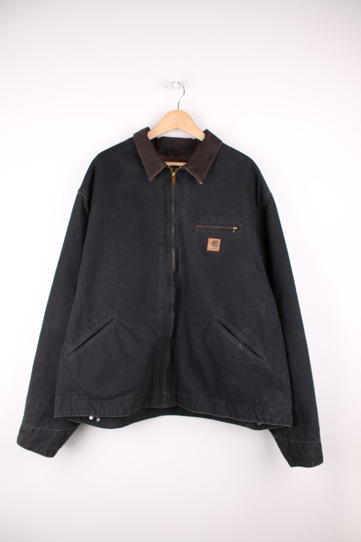 Carhartt Detroit Jacket in a black colourway with a brown corduroy collar, zip up with multiple pockets, blanket lining, and has the logo embroidered on the front. 