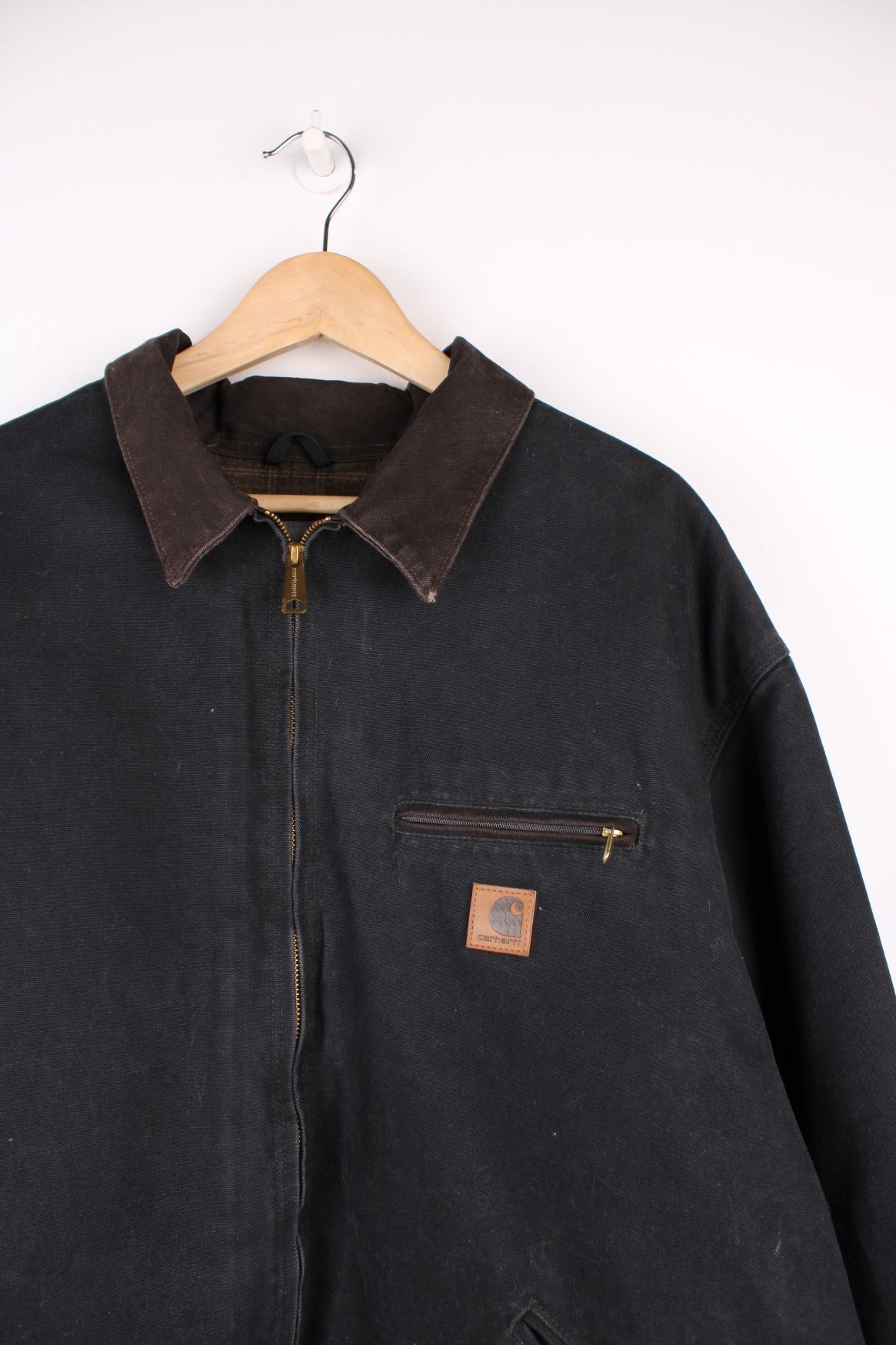 Carhartt Detroit Jacket in a black colourway with a brown corduroy collar, zip up with multiple pockets, blanket lining, and has the logo embroidered on the front. 