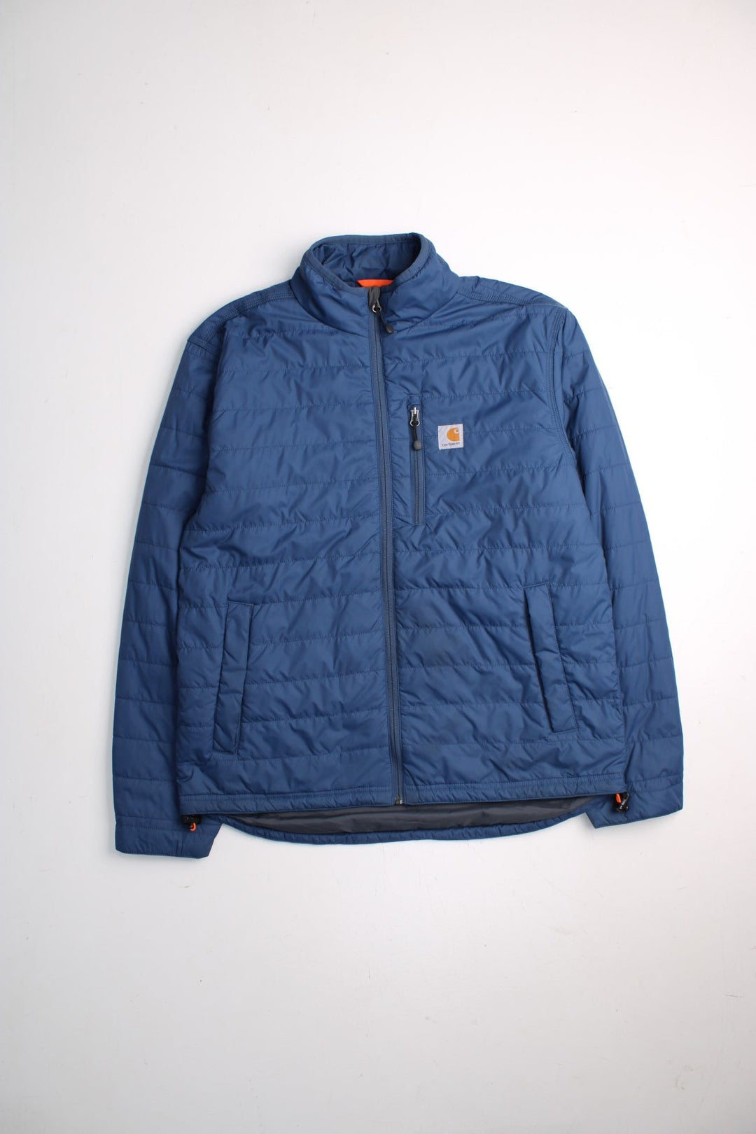 Carhartt Puffer Jacket in a blue colourway. Zips up and has multiple pockets, insulated, and has the logo embroidered on the front.