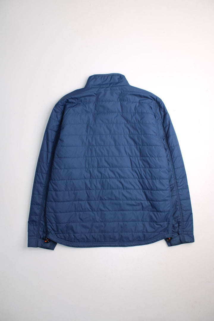 Carhartt Puffer Jacket in a blue colourway. Zips up and has multiple pockets, insulated, and has the logo embroidered on the front.