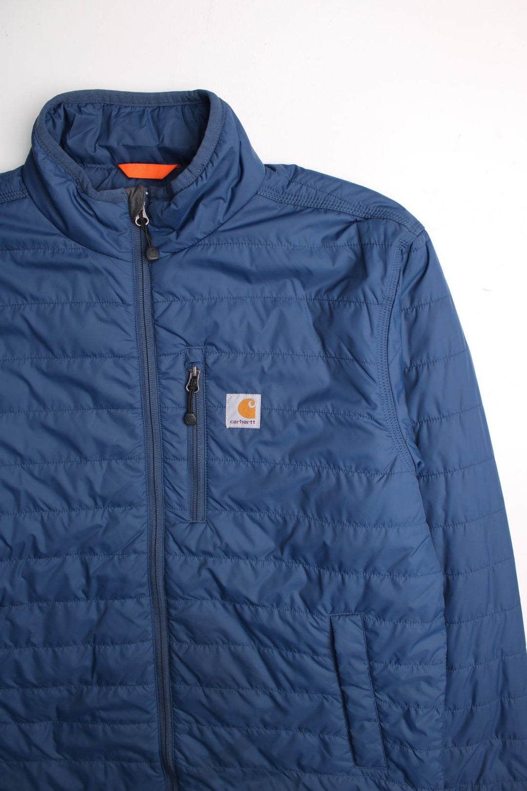 Carhartt Puffer Jacket in a blue colourway. Zips up and has multiple pockets, insulated, and has the logo embroidered on the front.