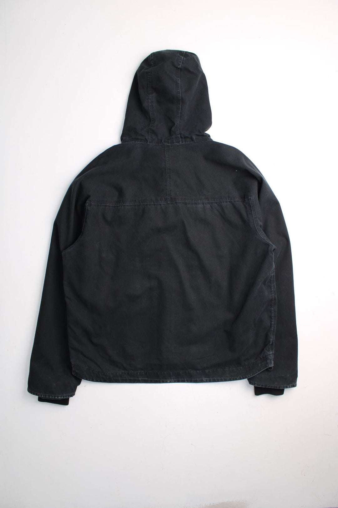 Carhartt Duck Canvas Workwear Jacket in a black colourway. Zip and button up with multiple pockets, reflective lining around the pockets, hooded, and has the logos embroidered on the front.