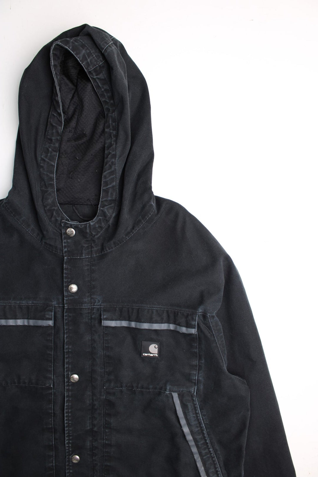 Carhartt Duck Canvas Workwear Jacket in a black colourway. Zip and button up with multiple pockets, reflective lining around the pockets, hooded, and has the logos embroidered on the front.