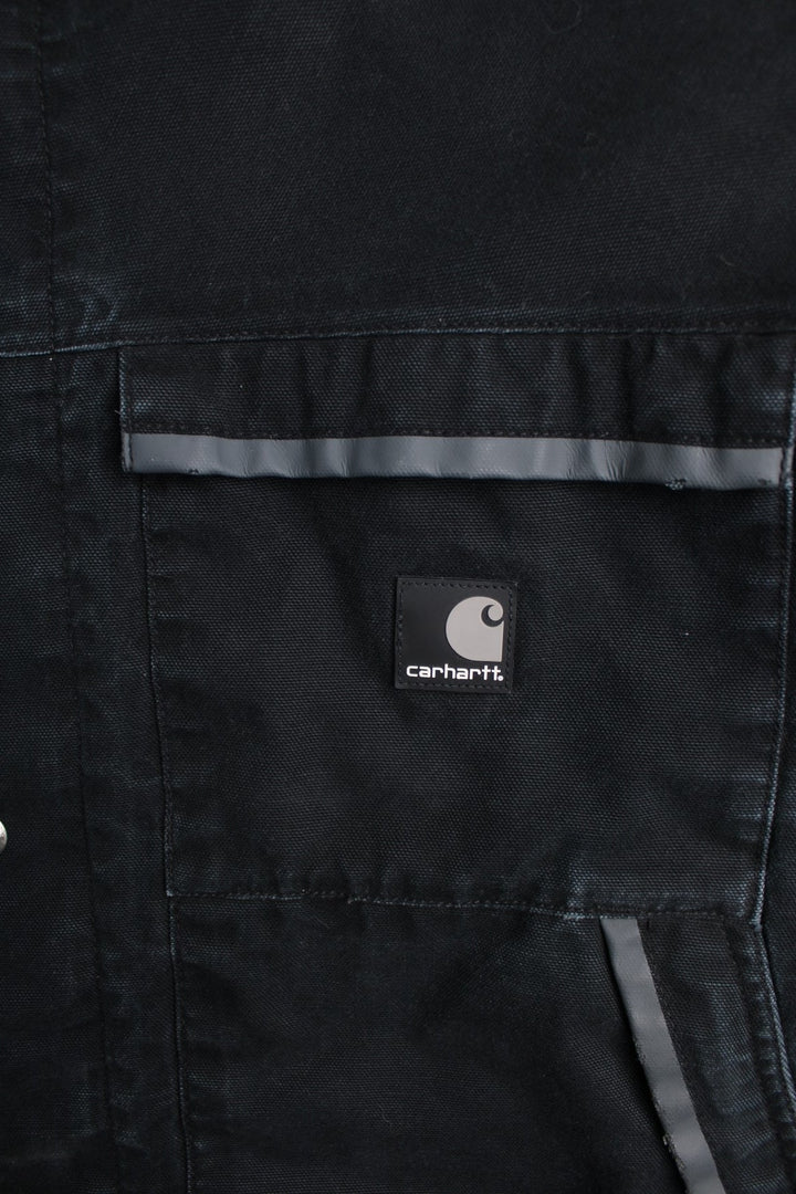 Carhartt Duck Canvas Workwear Jacket in a black colourway. Zip and button up with multiple pockets, reflective lining around the pockets, hooded, and has the logos embroidered on the front.